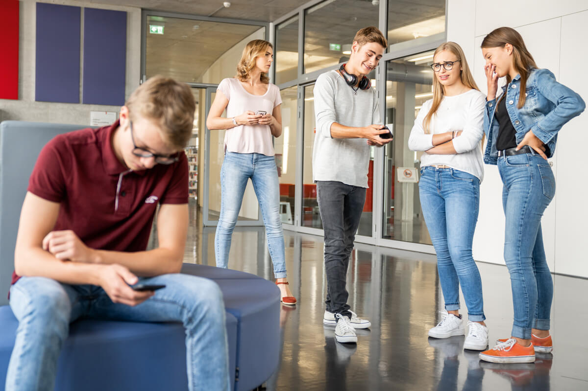 Gruppe jugendlicher macht sich über einen Mitschüler lustig, sie zeigen Bilder auf ihren Smartphones.