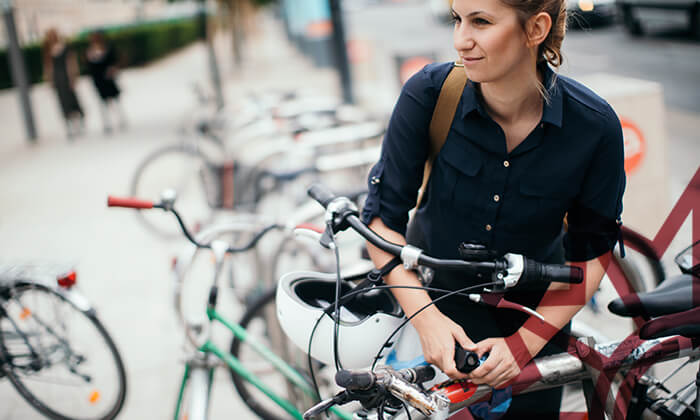 Frau schließt Fahrrad an Fahrradständer mit mehreren Fahrrädern an