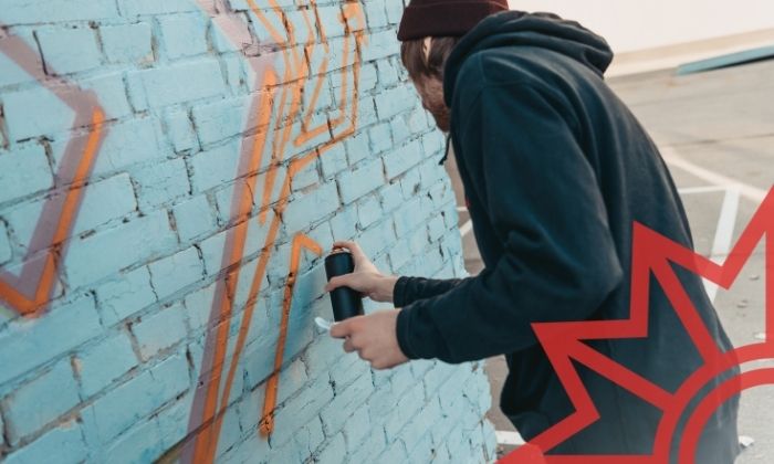 Junger Mensch sprüht Grafffiti an graue Hauswand